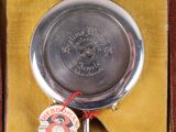 a silver pocket watch in a box with a tag on it