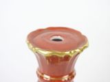 a red vase with a gold rim on a white surface