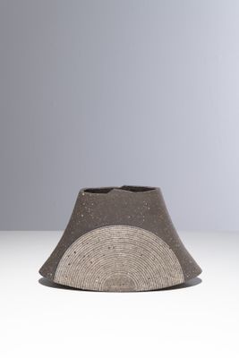 un vase gris et blanc posé sur une table blanche, sur fond gris