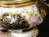 a woman holding a gold and black vase with flowers on it