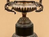 un vase en argent orné de deux oiseaux, posé sur un socle