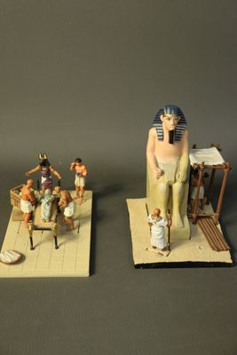 two figurines of pharaohs sitting on a rug next to a statue of a man