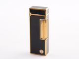 une image représentant un briquet noir et doré posé sur une surface blanche