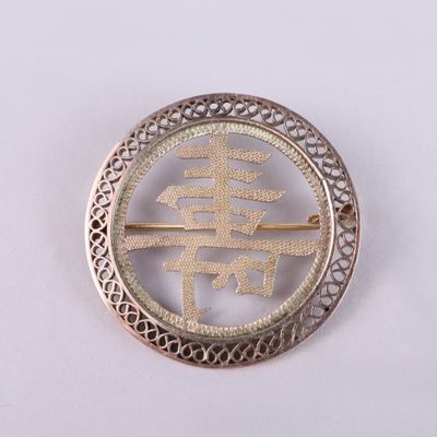 une image représentant une broche en argent sur laquelle figure un symbole chinois