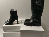 two pairs of black boots are sitting on top of a stack of white boxes