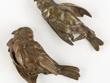 two bronze birds sitting on top of each other on a white surface