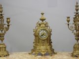 a gold clock sitting on top of a table next to three candles