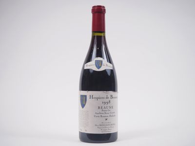 the bottle of red wine is sitting on a white surface