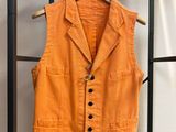 Un gilet orange est suspendu à un porte-vêtements devant un mur blanc.