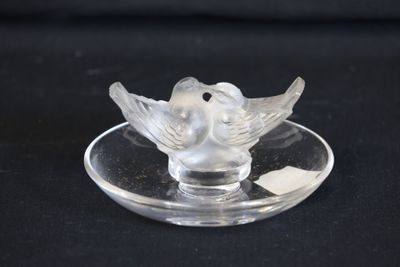 un oiseau en verre posé sur une assiette en verre, sur fond noir