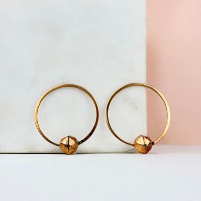 une paire de boucles d'oreilles créoles en or posée sur une dalle de marbre