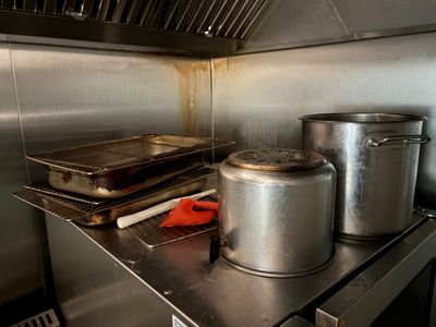 Des casseroles et des poêles sont posées sur un plan de travail en acier inoxydable dans une cuisine professionnelle.