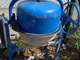 une bétonnière bleue posée par terre à côté d'une clôture