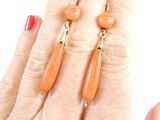 pair of orange earrings on a woman ' s hand with a red manicure