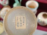 a person holding a plate with asian writing on it in front of a shelf of vases