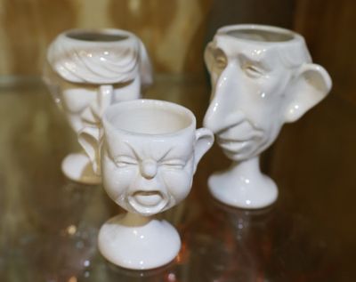 trois vases blancs ornés de visages, posés sur une table en verre
