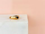 une bague en or sertie d'une pierre noire repose sur un bloc de marbre