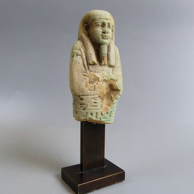 une statue égyptienne représentant un homme, dont la tête repose sur un socle en bois