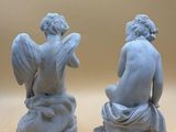 two statues of angels sitting on top of each other on a table
