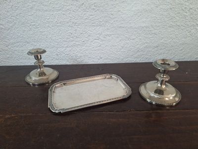 deux bougeoirs en argent et un plateau posés sur une table