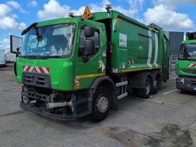 two green garbage trucks parked in a parking lot next to each other