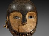 un gros plan d'un masque en bois posé sur un socle, sur une surface blanche