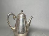 an antique silver tea pot with a handle on a gray surface