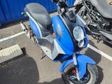 un scooter bleu garé sur un parking à côté d'une moto