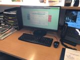 a desk with a computer monitor, keyboard, phone, and other items on it