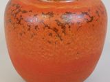 a small orange vase sitting on a white surface