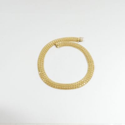 un bracelet en or posé sur une surface blanche, sur fond blanc