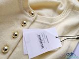 a white sweater with gold buttons and a tag on it