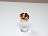 a gold ring with a red stone on top of a clear glass