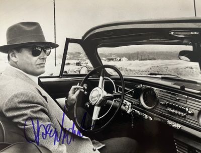 photographie en noir et blanc d'un homme assis dans une voiture, coiffé d'un fedora