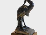 une image représentant une statue en bronze d'un oiseau posée sur un socle en bois