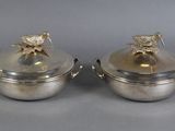 two silverplated dishes with lids and handles on a gray surface