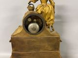 a gold clock with a lady sitting on top of it