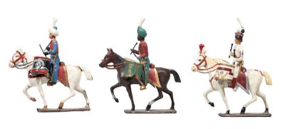 trois figurines représentant des hommes en uniforme à cheval, posées sur un fond blanc