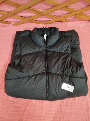 un gilet matelassé noir posé sur un lit recouvert d'une couverture rose