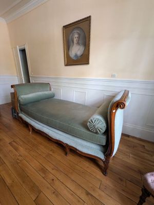 a chaise in the middle of a room with a painting on the wall