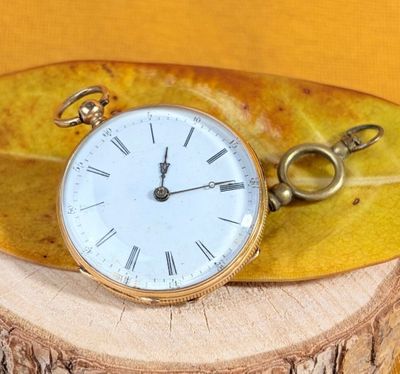 a gold pocket watch sitting on top of a leaf
