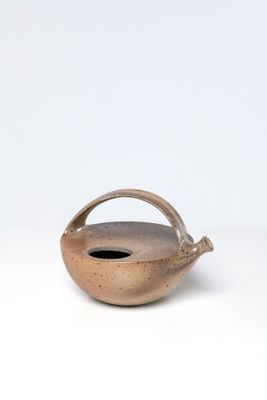 une image représentant un petit vase marron muni d'une anse, posé sur une surface blanche