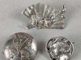 trois broches en argent et un éventail posés sur un fond blanc