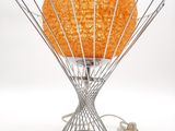 une lampe orange posée sur un pied en fil de fer