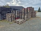 de nombreuses palettes empilées au sol devant un bâtiment