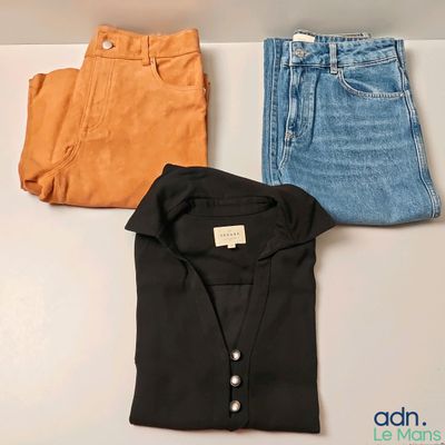 trois paires de jeans et une chemise posées sur une table