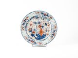 assiette bleue et blanche ornée de fleurs orange sur un socle, sur fond blanc