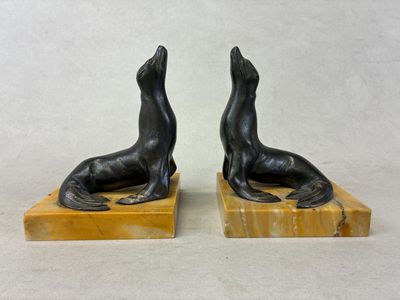 une paire de serre-livres en bronze représentant des otaries, posés sur des socles en marbre