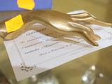 une statue en or représentant une main tenant un bout de papier sur une table en verre