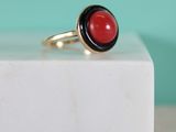bague en pierre noire et rouge posée sur un bloc de marbre blanc